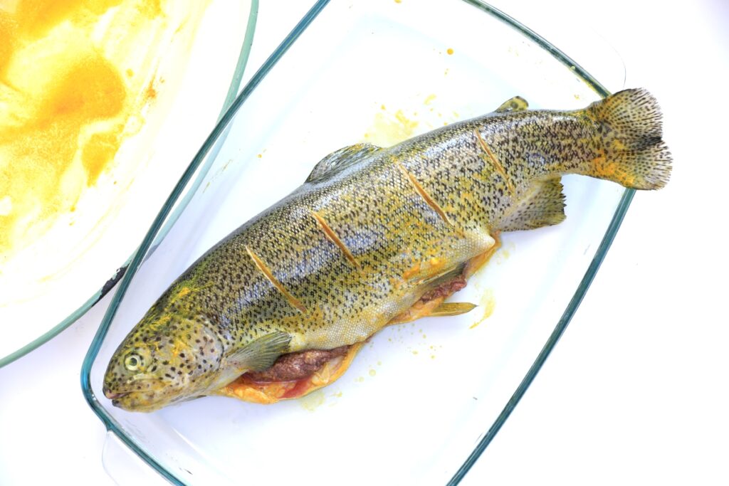 A fish on a plate beside a bowl of vibrant orange sauce