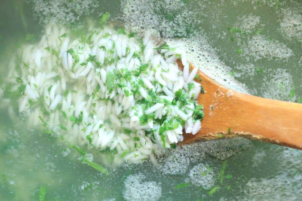 A wooden spoon scoops up a mixture of rice and herbs from a bowl