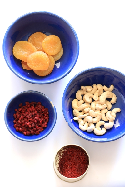 three bowls filled with plums, cashews, barberries, and a saffron container