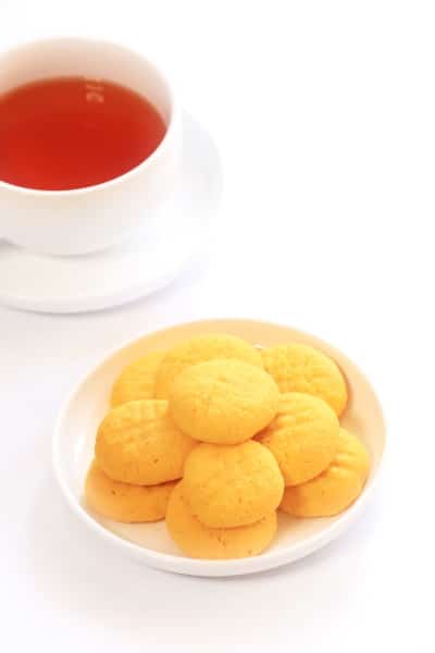 a plate of saffron cookies beside a steaming cup of tea