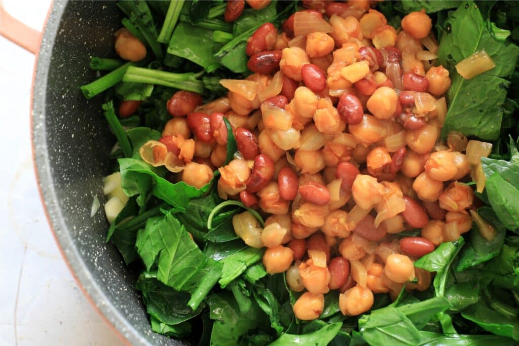 A pan filled with cooked beans and fresh spinach