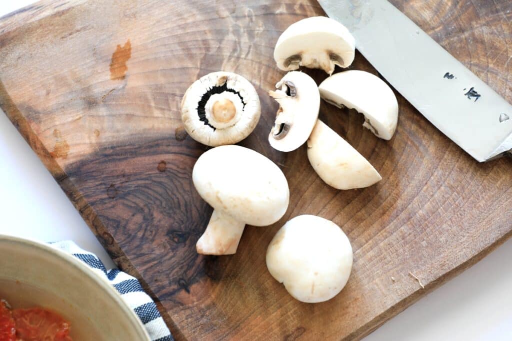 Mushrooms and ripe tomatoes arranged on a wooden cutting board, ready for preparation in a kitchen setting.
