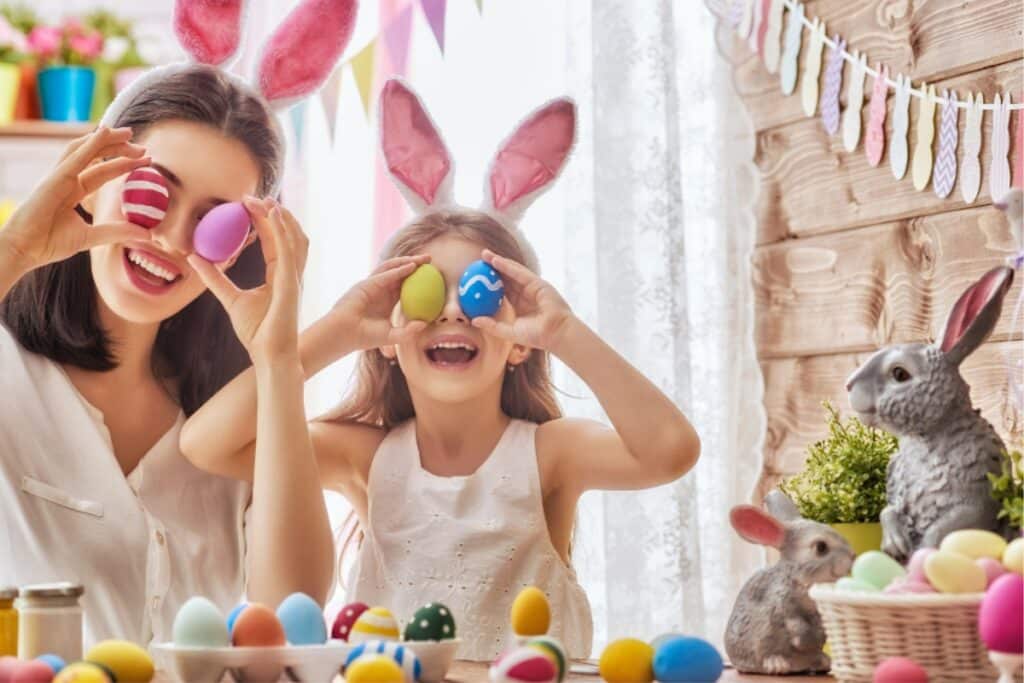 A woman and two children joyfully hold colorful Easter eggs, smiling in a bright outdoor setting.