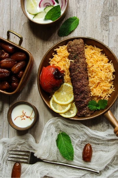 A plate of kebab served with rice and dates, placed on a rustic wooden table.