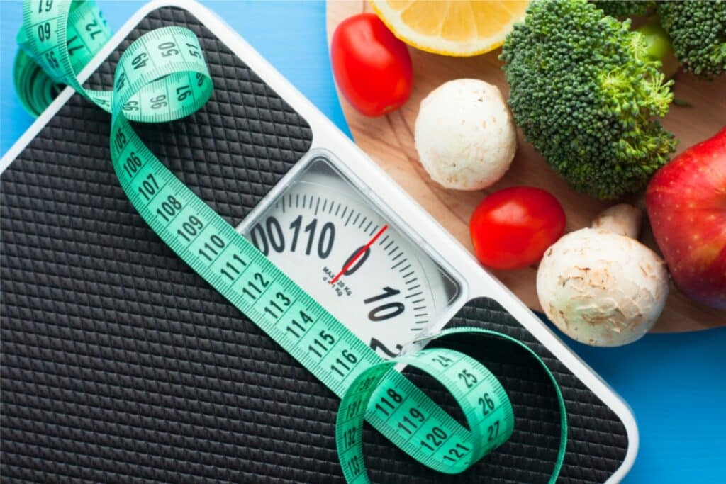 Healthy food items and a weight scale on a blue background, illustrating a weight loss concept.