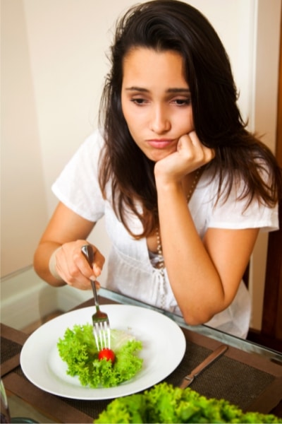 A woman gazes thoughtfully at a colorful plate of fresh salad, contemplating her meal choice.