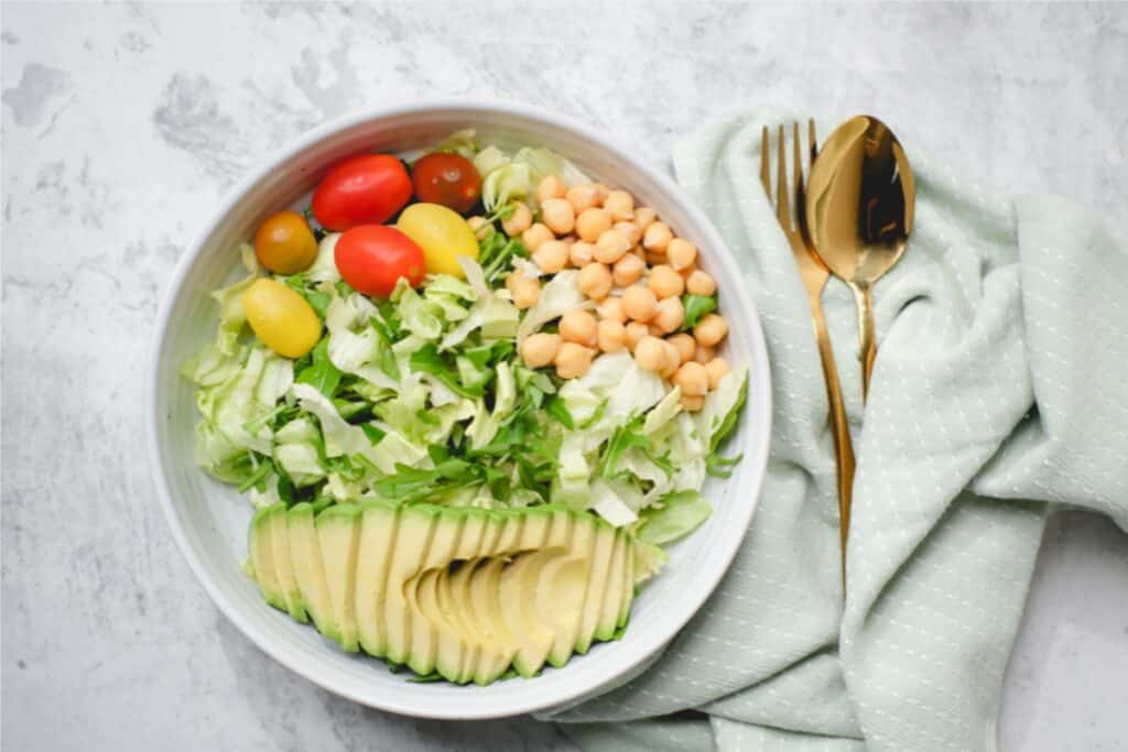 A bowl of salad featuring avocado, tomatoes, and chickpeas, arranged attractively for a fresh and healthy meal.