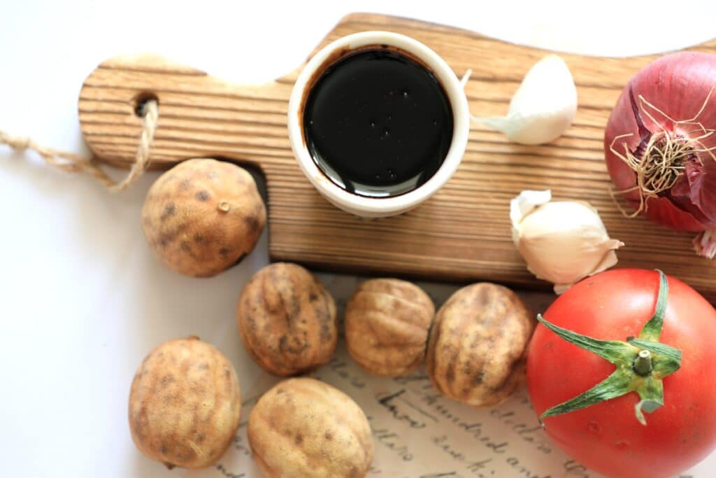 A wooden cutting board displaying a cup of coffee, fresh tomatoes, and walnuts arranged neatly.