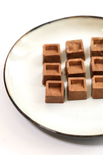 A white plate filled with several dark chocolate squares arranged neatly.