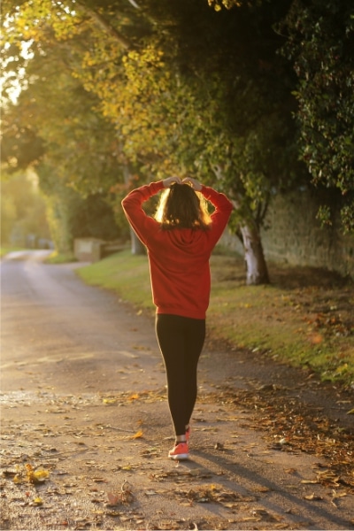 A woman in a red sweater walking along a road surrounded by trees and greenery.
