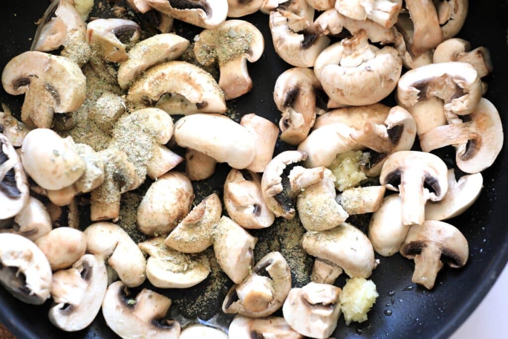 Mushrooms sautéing in a skillet, seasoned with various spices, creating a flavorful dish.