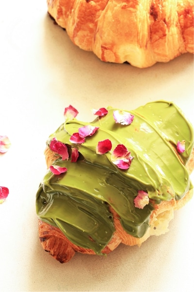 Pastry topped with green icing and adorned with delicate pink petals.