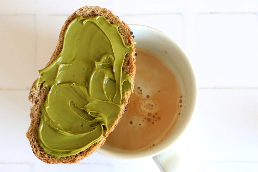 A cup of coffee beside a slice of bread topped with fresh avocado.