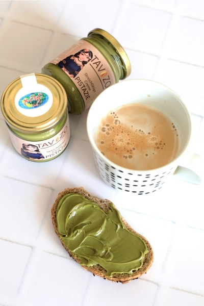 A cup of coffee beside a jar of creamy avocado spread on a wooden table.