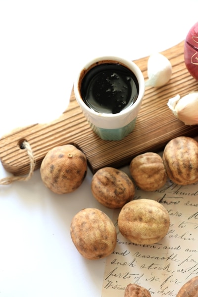 A wooden cutting board displaying an assortment of nuts, garlic cloves, and a small bottle of oil.