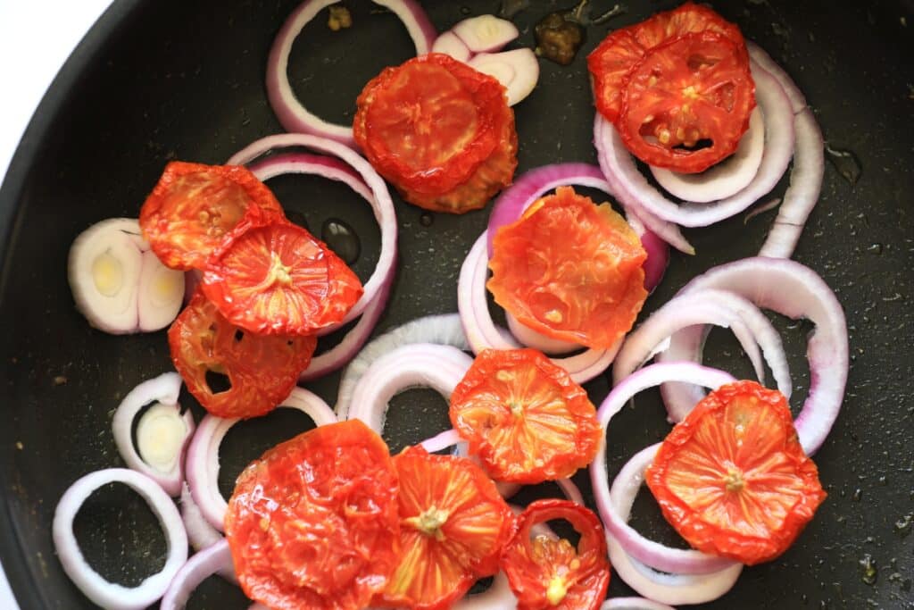 A pan with diced tomatoes and onions sizzling as they cook together on a stovetop.
