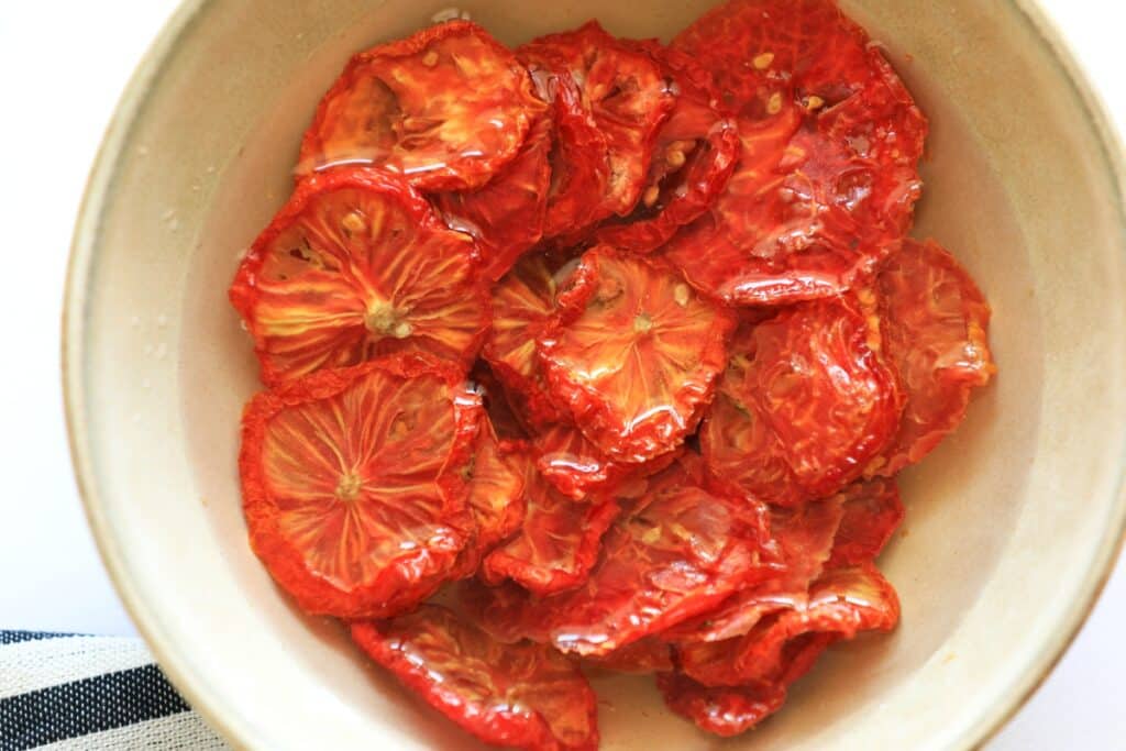 A bowl of sliced tomatoes sits on a white table, showcasing vibrant red and green colors against a clean background.