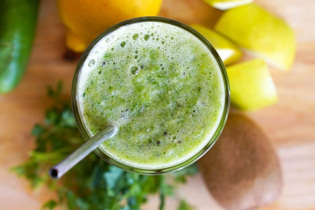 A vibrant green smoothie featuring cucumbers, kiwi, and lemon, served in a clear glass.