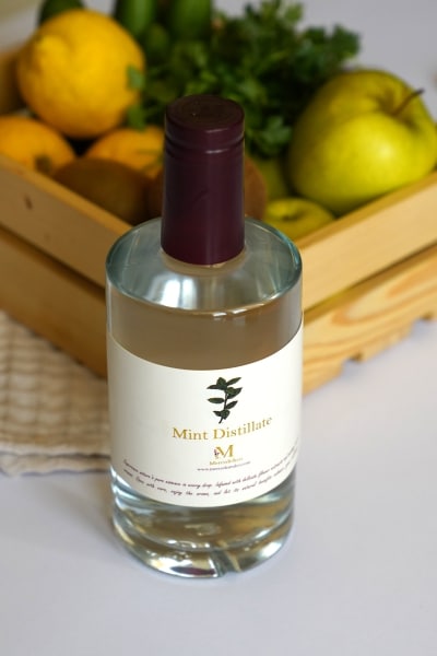 A bottle placed beside a colorful basket filled with assorted fresh fruits.