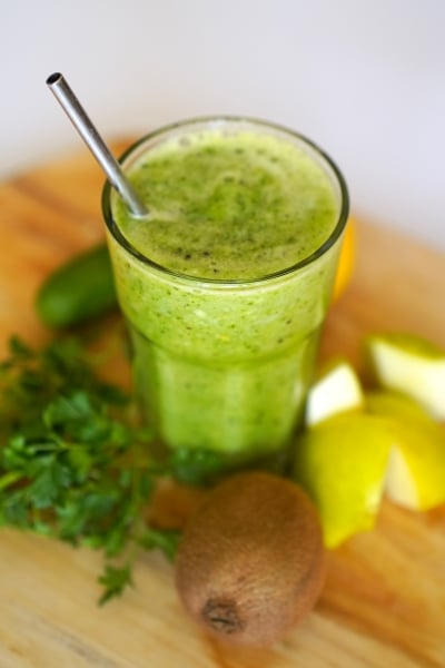 A vibrant green smoothie featuring cucumbers, kiwi, and lemon, served in a clear glass.